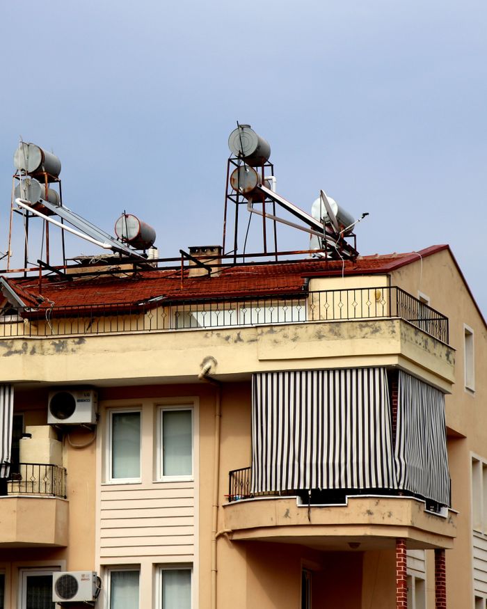 services-01 A close-up view of an urban residential building featuring solar water heaters on the rooftop.
