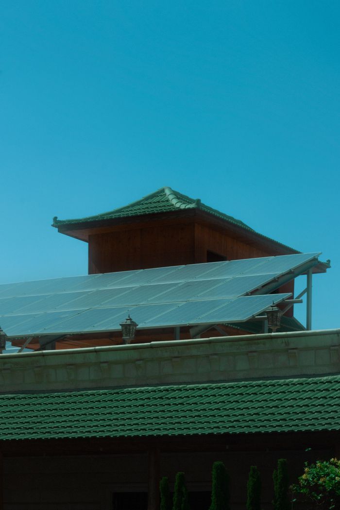 about-us-01 A traditional pagoda with modern solar panels under a clear blue sky.